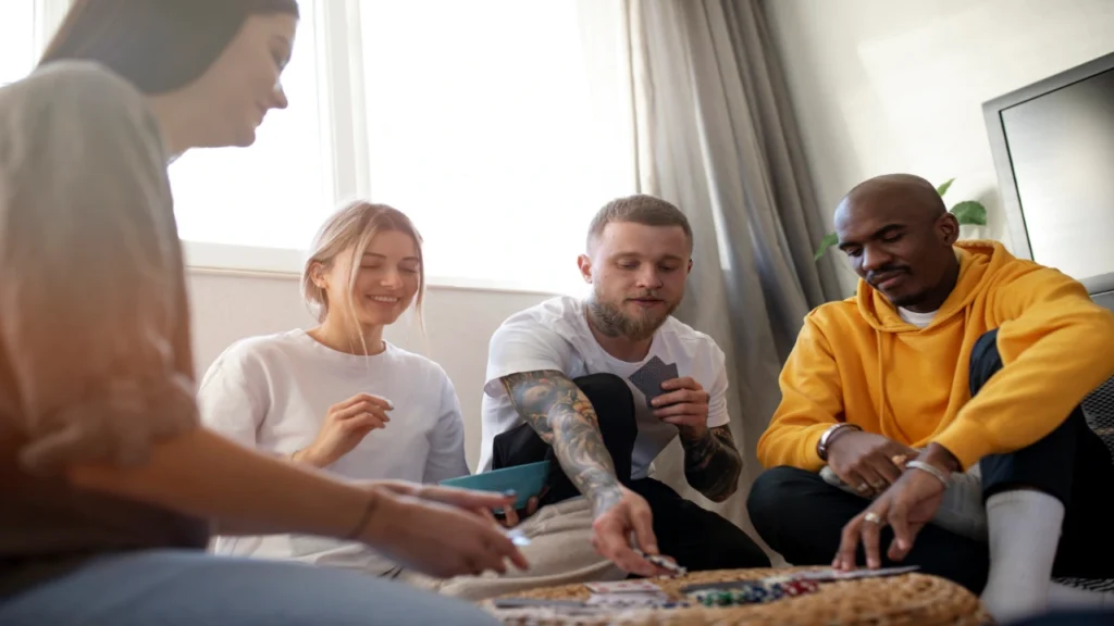 A diverse group of young adult friends smiling and playing a tabletop game together in a cozy room, perfect for hosting a night of Truth or Dare Questions.