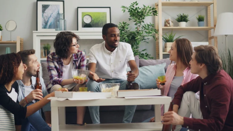 A group of young men and women talking and laughing on a couch during a house party, showcasing a perfect setting for Truth or Dare Questions.