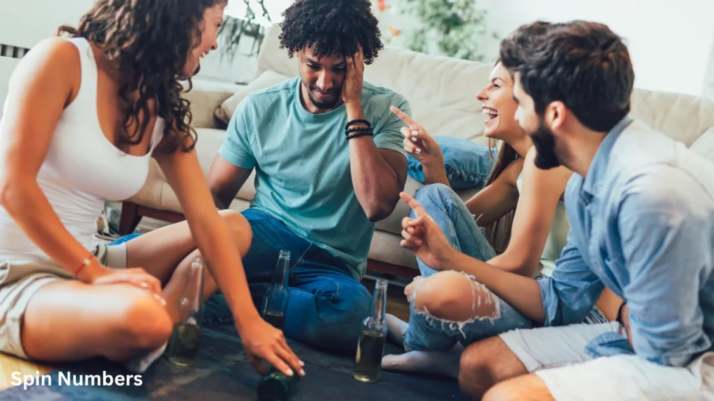 A group of young friends laughing and pointing at a young man holding his head while playing a lively session of Truth or Dare Questions.