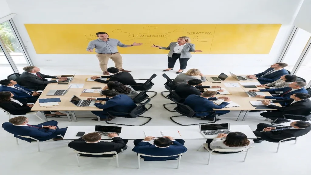 An aerial view of a corporate training room with professionals split into structured team tables to evaluate Random vs Self Selected Groups.