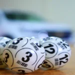 Numbered lottery balls resting on a table with a giveaway car prize blurred in the background of a Fair Raffle draw.