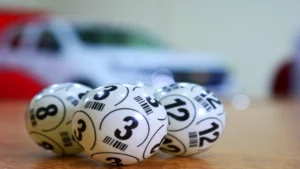 Numbered lottery balls resting on a table with a giveaway car prize blurred in the background of a Fair Raffle draw.