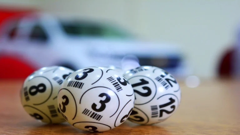 Numbered lottery balls resting on a table with a giveaway car prize blurred in the background of a Fair Raffle draw.