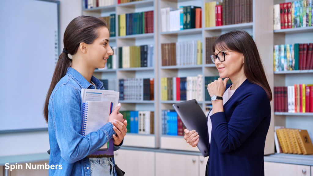 A high school teacher talking to a female student holding notebooks to encourage classroom student participation.