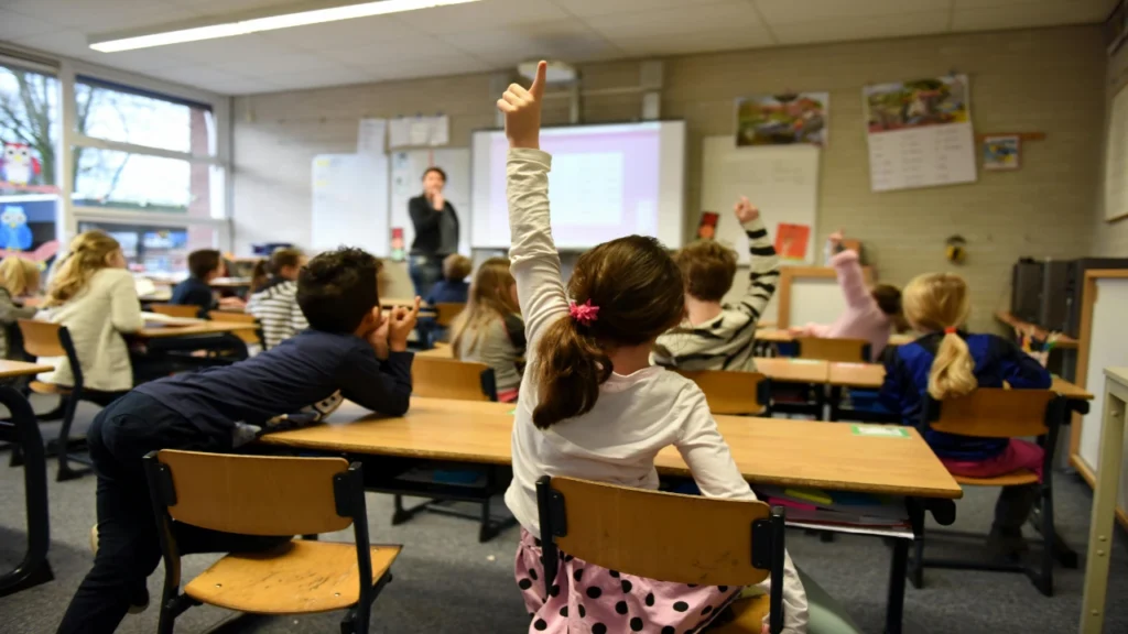 An eager student raising her hand high next to a disengaged peer, demonstrating the necessity of Cold Calling in the Classroom.