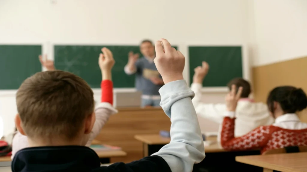 Students raising their hands in front of a green chalkboard, contrasting traditional calling with effective Cold Calling in the Classroom.